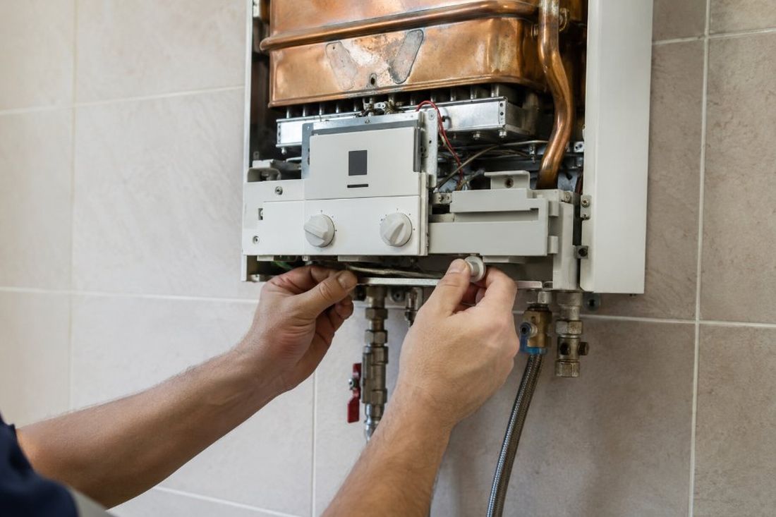 Manos reparando el interior de un calentador de gas